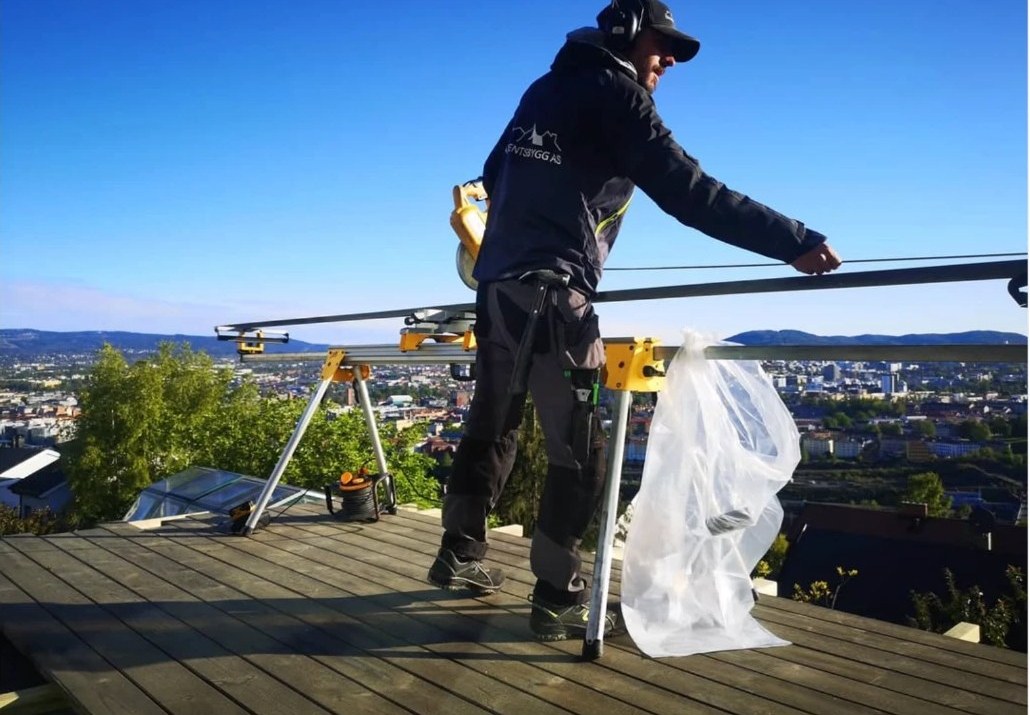 Tømrer fra Barentsbygg AS kutter terrassebord med utsikt over Oslo